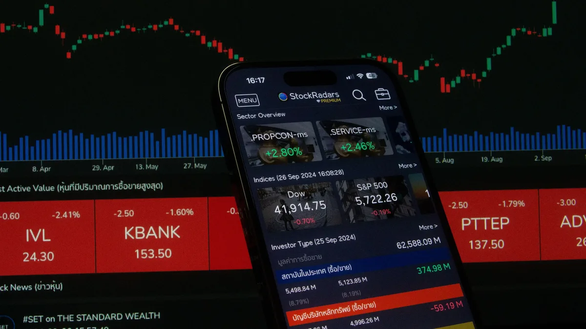 A smartphone displaying a stock market app, with a graph and stock prices visible on the screen.